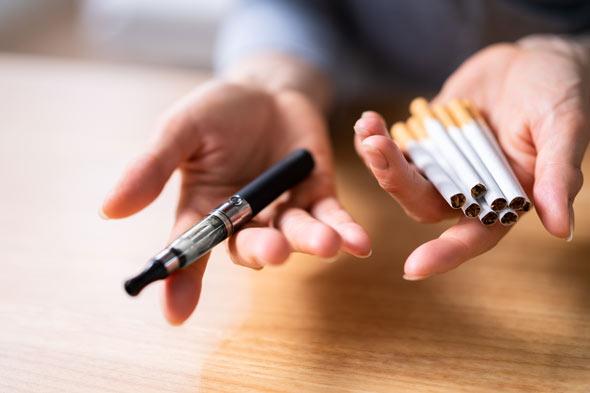 A person holding a vape and cigarettes